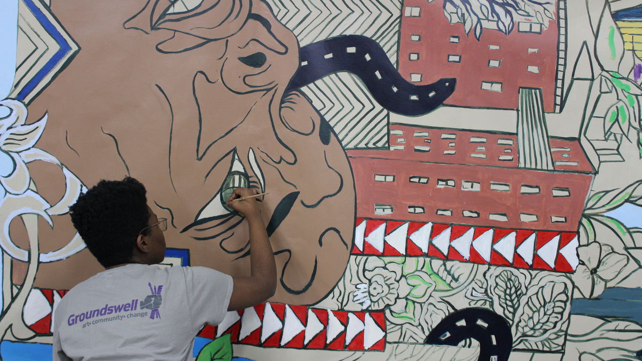 A youth artist wears a Groundswell branded t-shirt as she paints a mural.