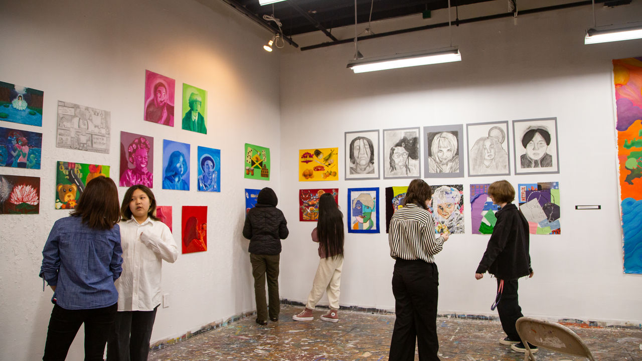 People walking around exhibition looking at various art on the wall 