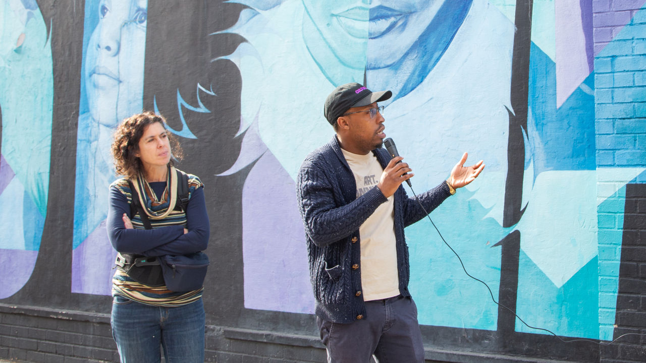 Two presenters talking about the artwork behind them 