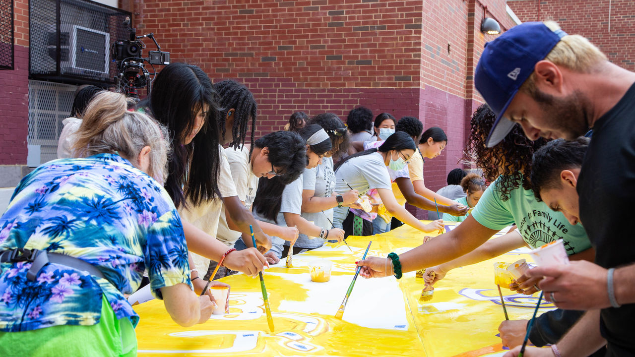 Group of people painting a mural on parachute cloth placed on a table. 