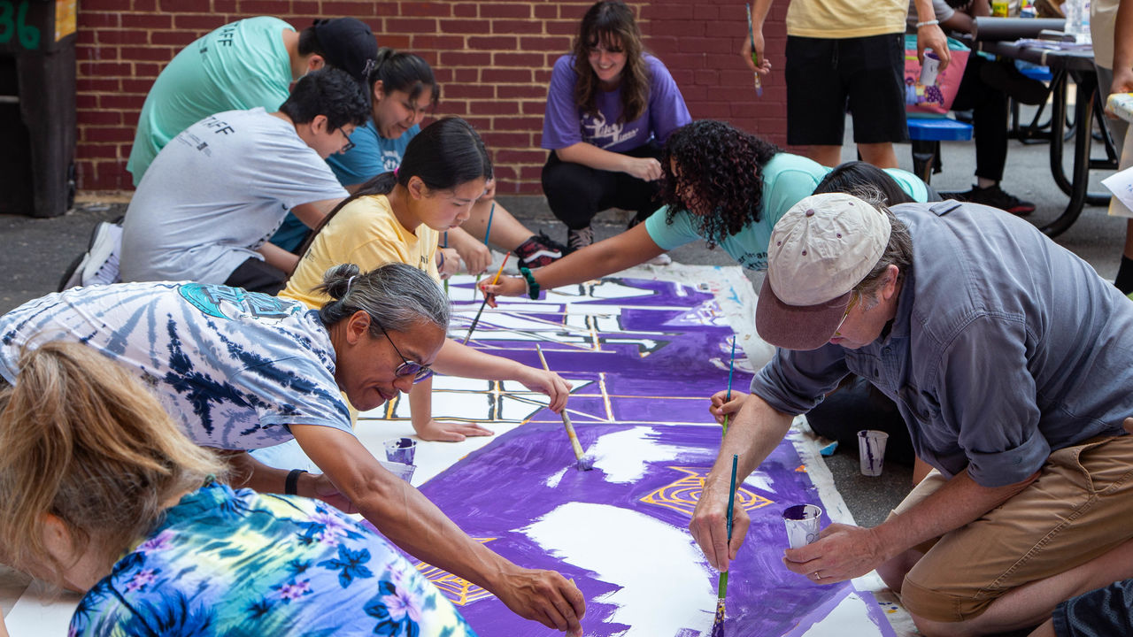 Group of people painting a mural on parachute cloth placed on the ground. 