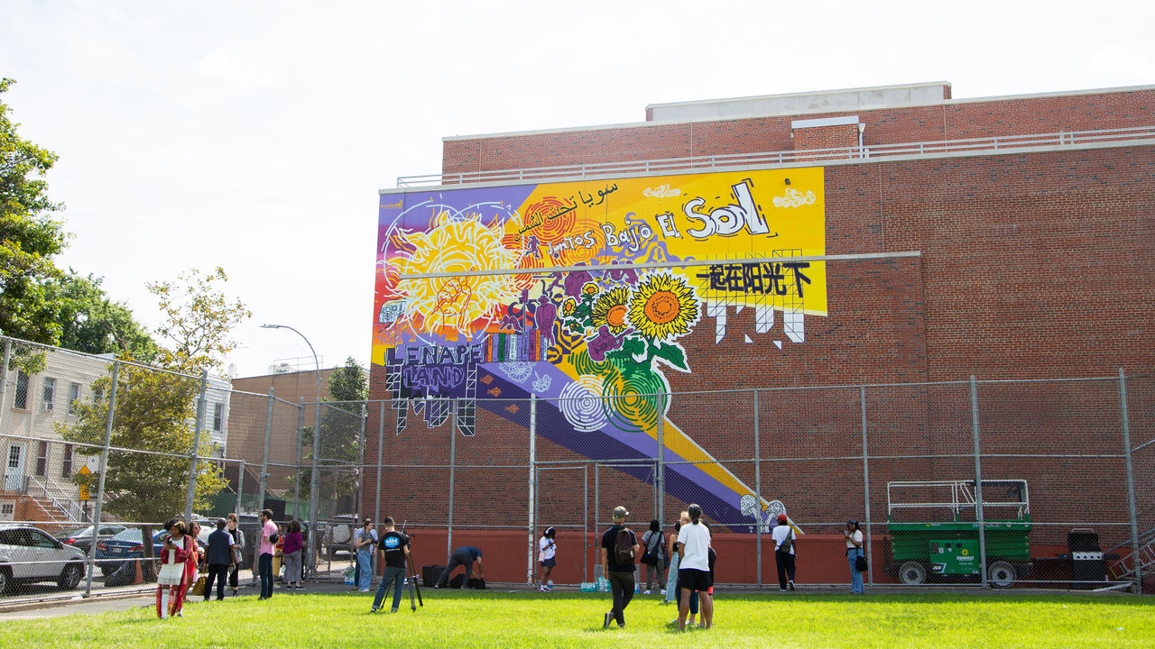 Wide photo of completed mural on a high wall with people admiring it from below.
