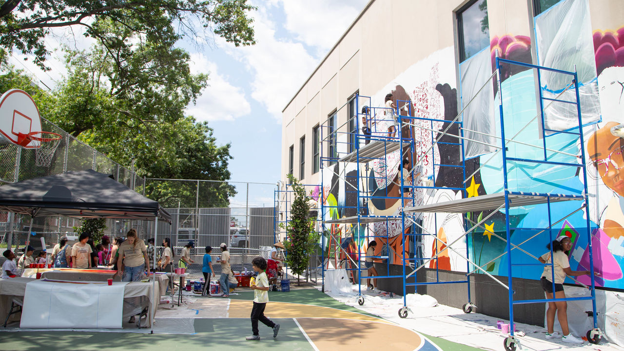 Wide shot of scaffolding against the wall to paint a big mural on the right side and a tent set up on the left side