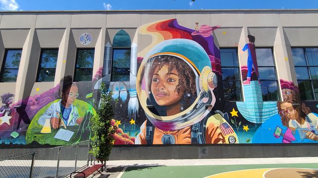 Photo of mural on wall with different designs like an astronaut, a girl making a robot, a girl doing a science experiment. 