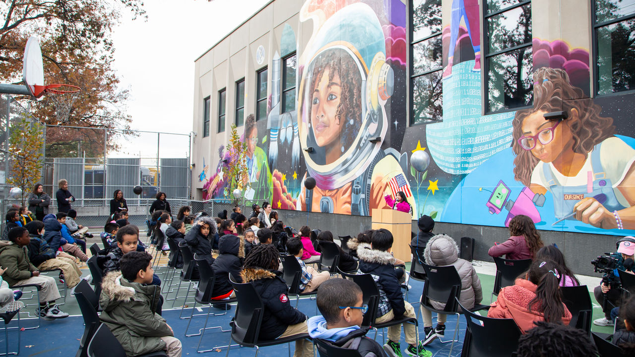 Group of students listening to presenter talk about mural behind her. 