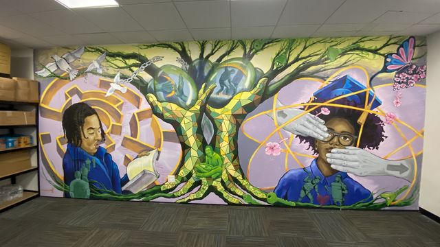 Mural featuring a tree with branches, a maze, a figure reading and a figure in a graduation outfit with two hands covering an eye and their mouth
