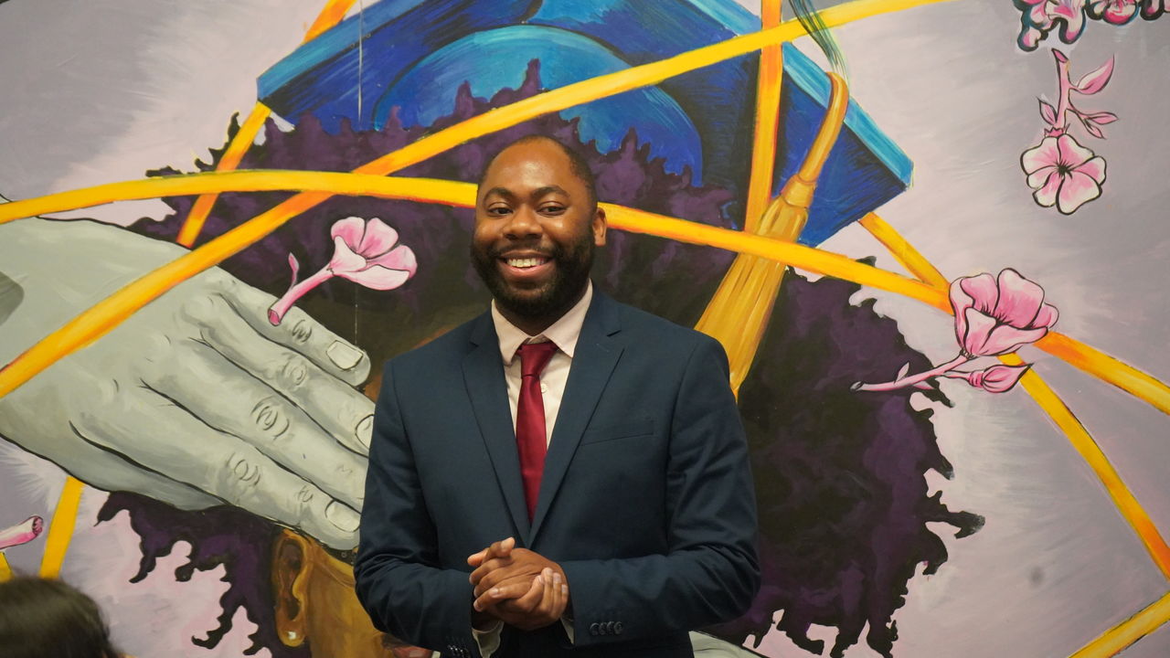 Photo of presenter speaking in front of mural art. 