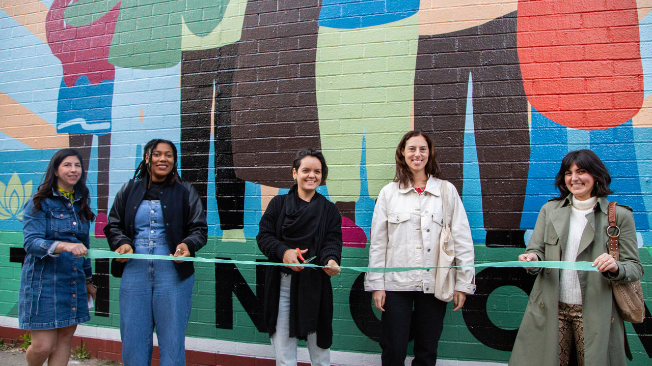 People standing in front of a mural doing a ribbon cutting ceremony. 