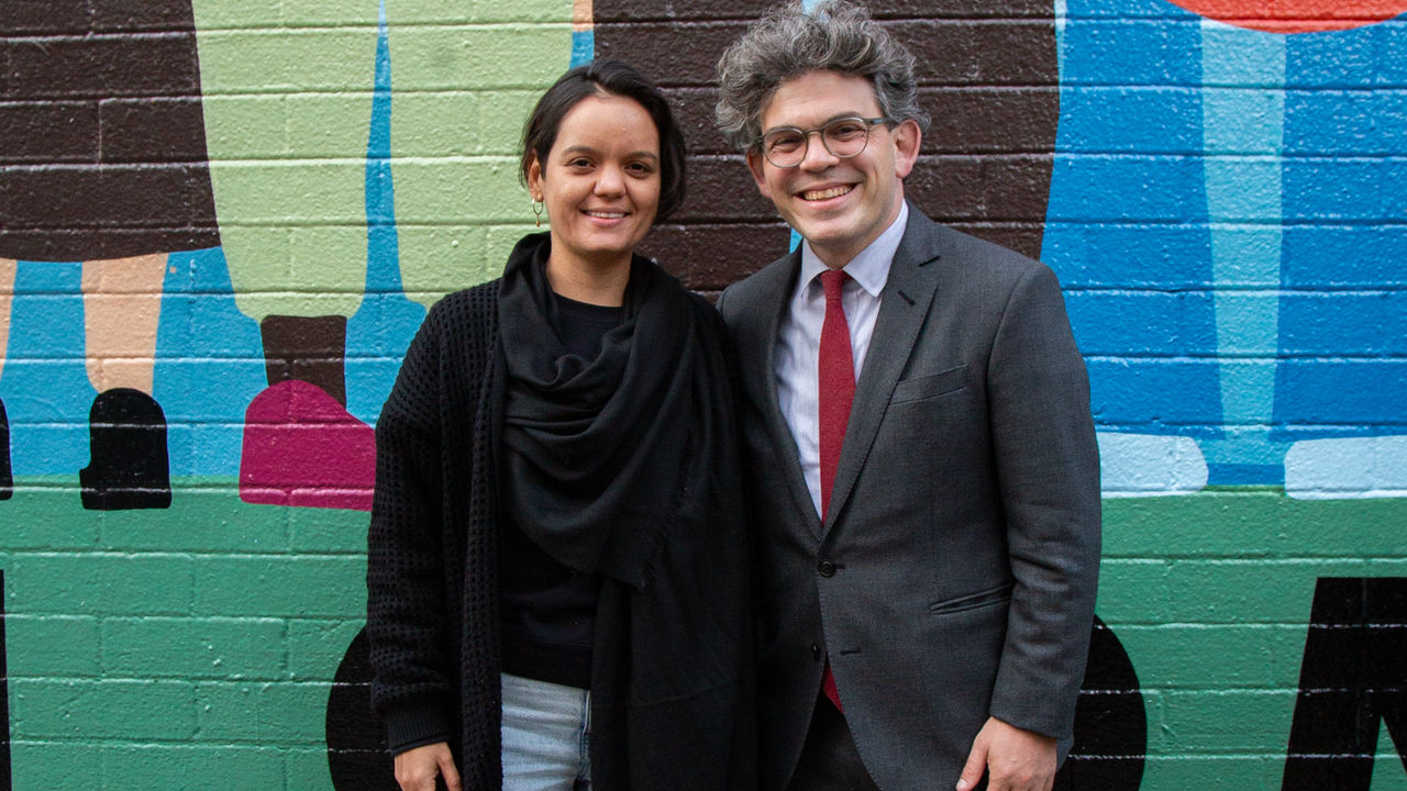 Two people smiling in front of a mural. 