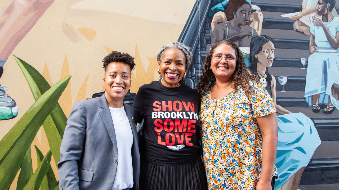 Three people posing in front of mural 