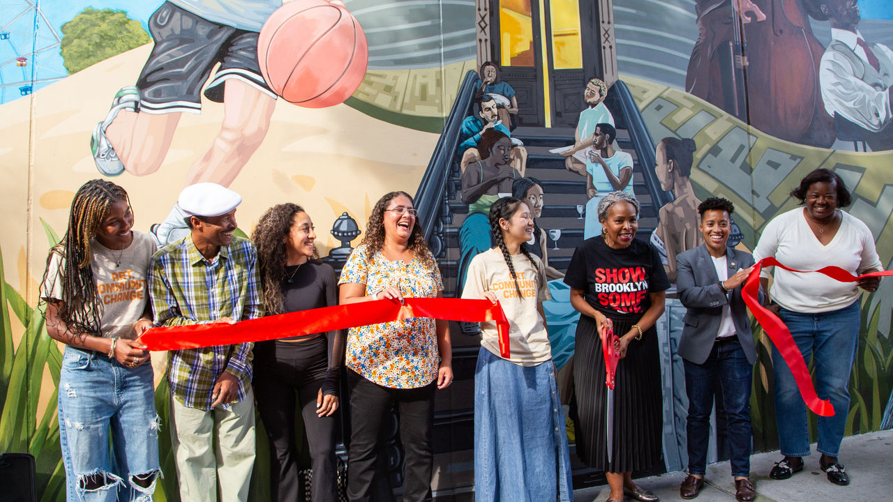 People standing in front of mural doing a ribbon cutting ceremony 