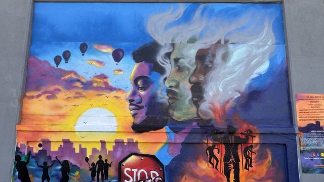 Mural showing 3 figures, 2 of them in smoke, a sunset, figures playing, a sign that says "stop lies" and a puppeteer. 