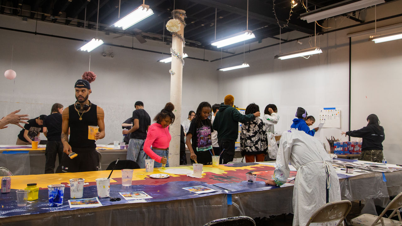 Room of people painting a mural on parachute cloth on a table 