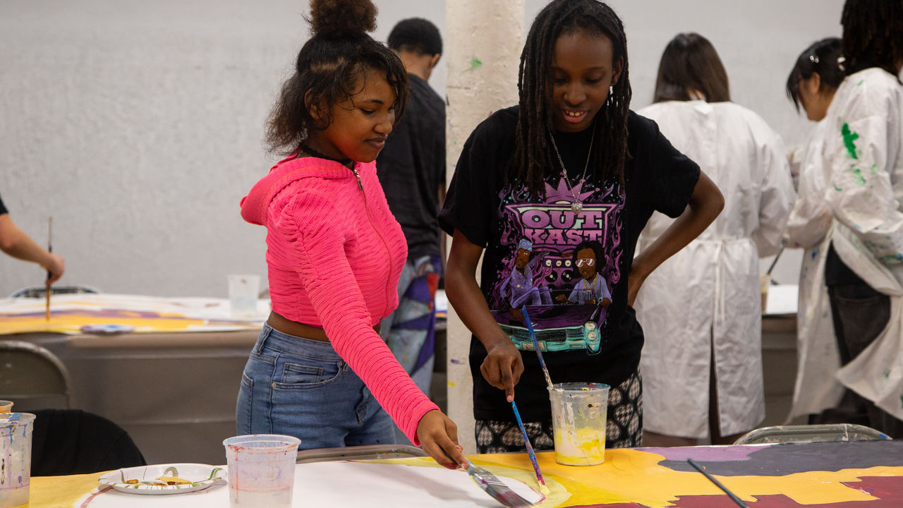 Two students painting mural on parachute cloth on a table. 