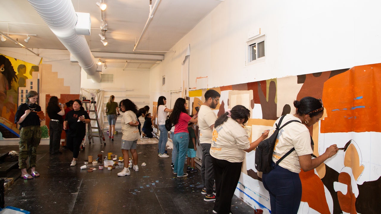Room full of people painting a mural on parachute cloth. 
