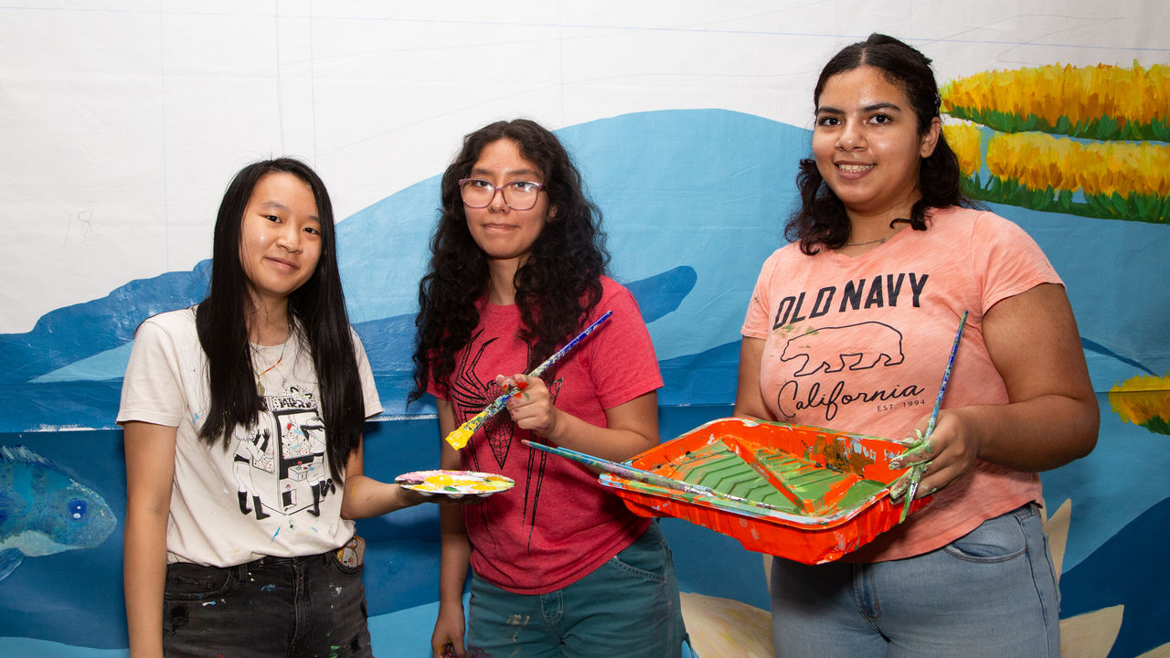 Three students posing with paint and brushes. 