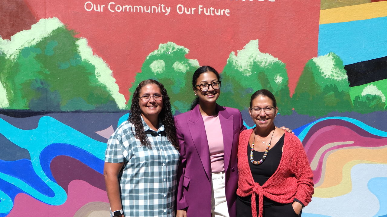 Group of three people posing in front of a mural 