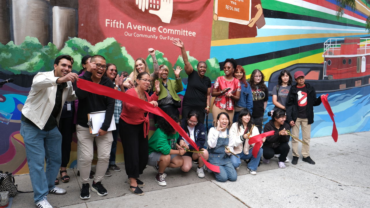 Group of people in front of a mural doing a ribbon cutting ceremony