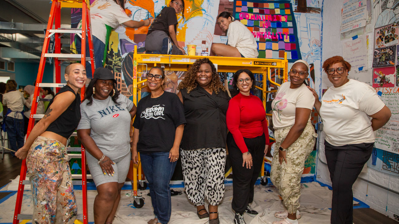 Group of people posing in front of a mural 
