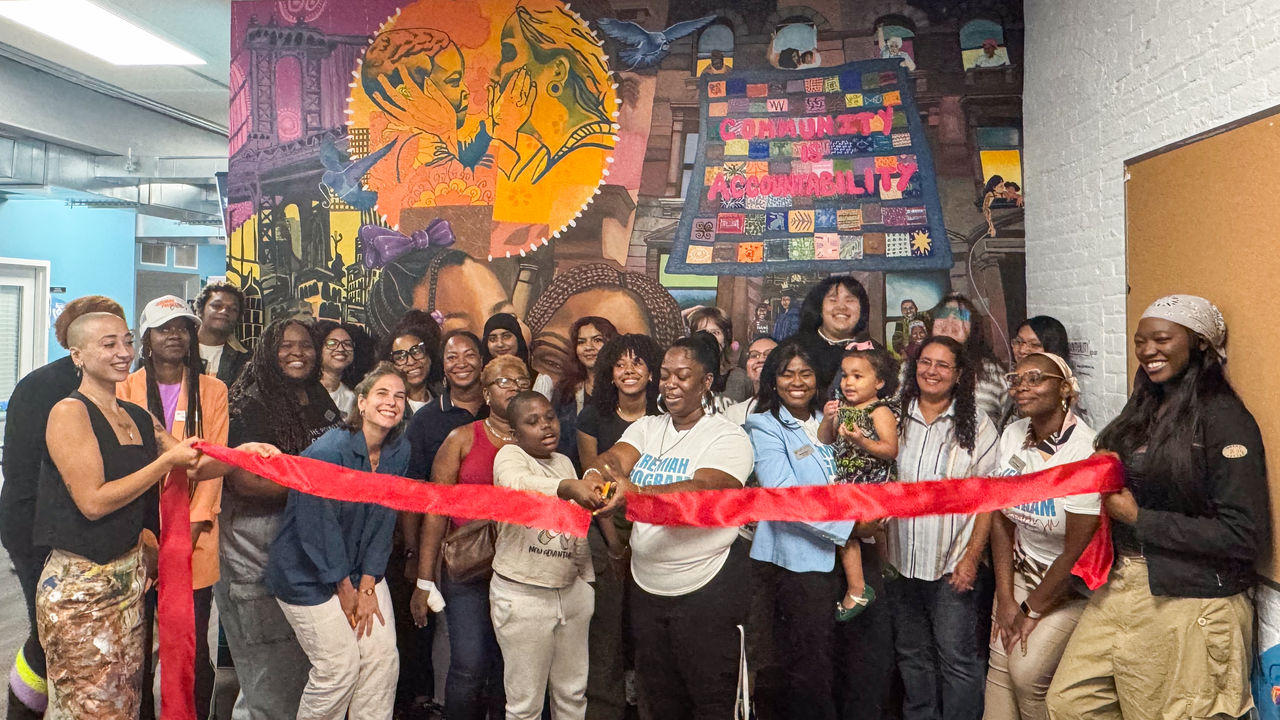 Group of people posing in front of a mural doing a ribbon cutting ceremony 