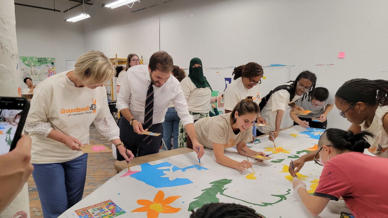 People surrounding a table to paint a mural on parachute cloth 