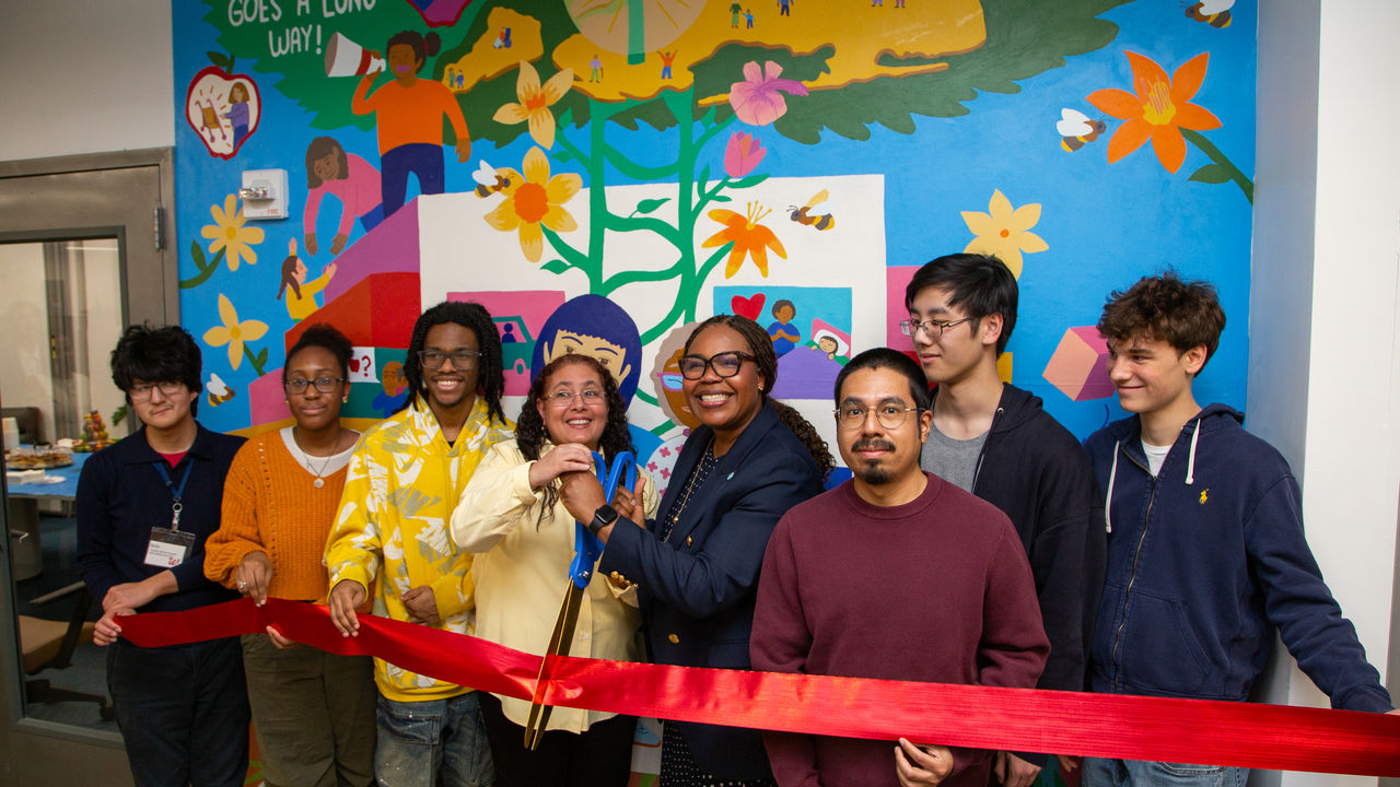 A group of people posing in front of a mural doing a ribbon cutting