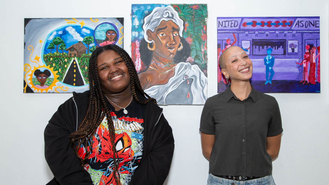 Teacher and student smiling posing in front of hanging artwork 