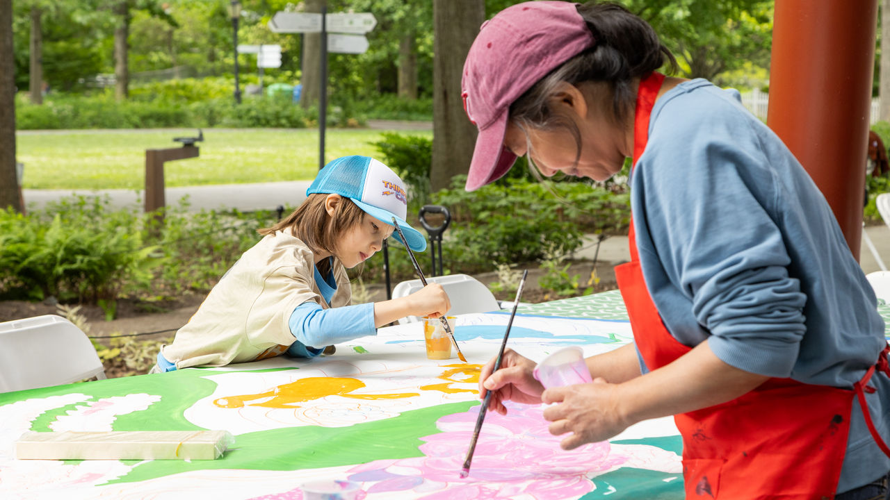 Child and adult painting a canvas 