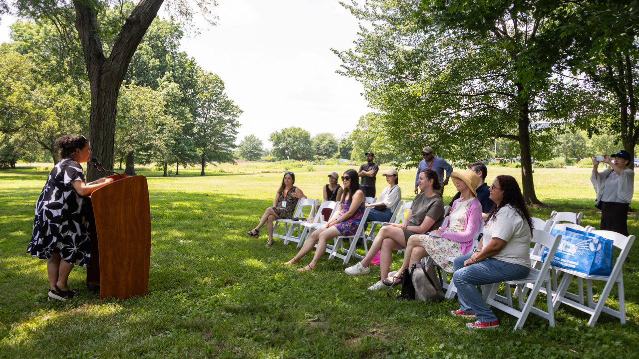 Group of people sitting and listening to a person speaking at a podium 