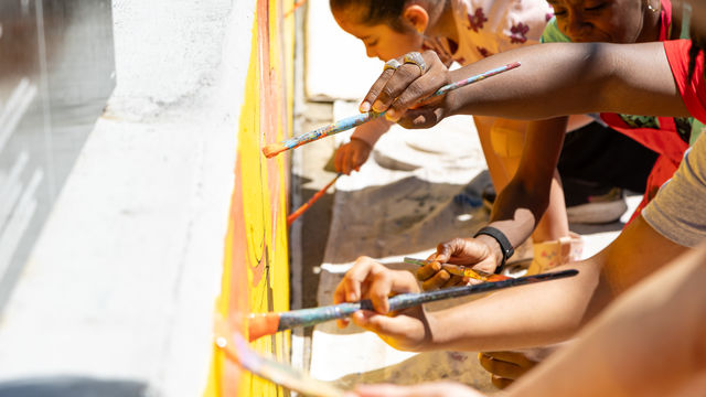 Multiple hands painting a mural on a wall